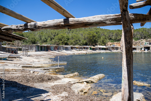 «Ibiza, Spain»; May 26 2026: Sa Caleta traditional fisherman huts and rustic wooden docks in a narrow rocky bay, showcasing the historic coastal heritage and turquoise Mediterranean sea.