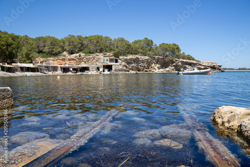 «Ibiza, Spain»; May 26 2026: Sa Caleta traditional fisherman huts and rustic wooden docks in a narrow rocky bay, showcasing the historic coastal heritage and turquoise Mediterranean sea.