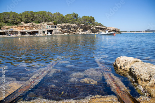 «Ibiza, Spain»; May 26 2026: Sa Caleta traditional fisherman huts and rustic wooden docks in a narrow rocky bay, showcasing the historic coastal heritage and turquoise Mediterranean sea.