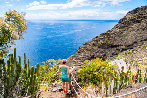 Hiker stands at a scenic overlook with rope railings, looking out at a winding trail and the blue ocean at Poris de la Candelaria, La Palma, Canary Islands, Spain