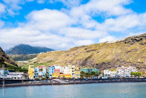 Vibrant coastal resort with colourful buildings sits along a black sand beach under a blue sky in Tazacorte town, La Palma, Canary Islands, Spain