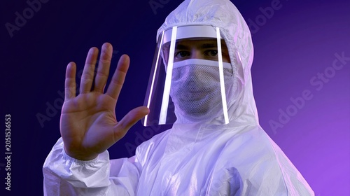 Close up of man wearing white hazmat suit and face shield with hand raised