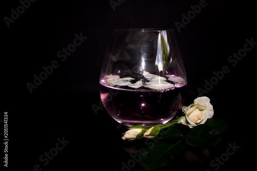 Foto A single glass of rose flavoured gin and tonic, garnished with rose petals, and rosebuds at the base of the glass