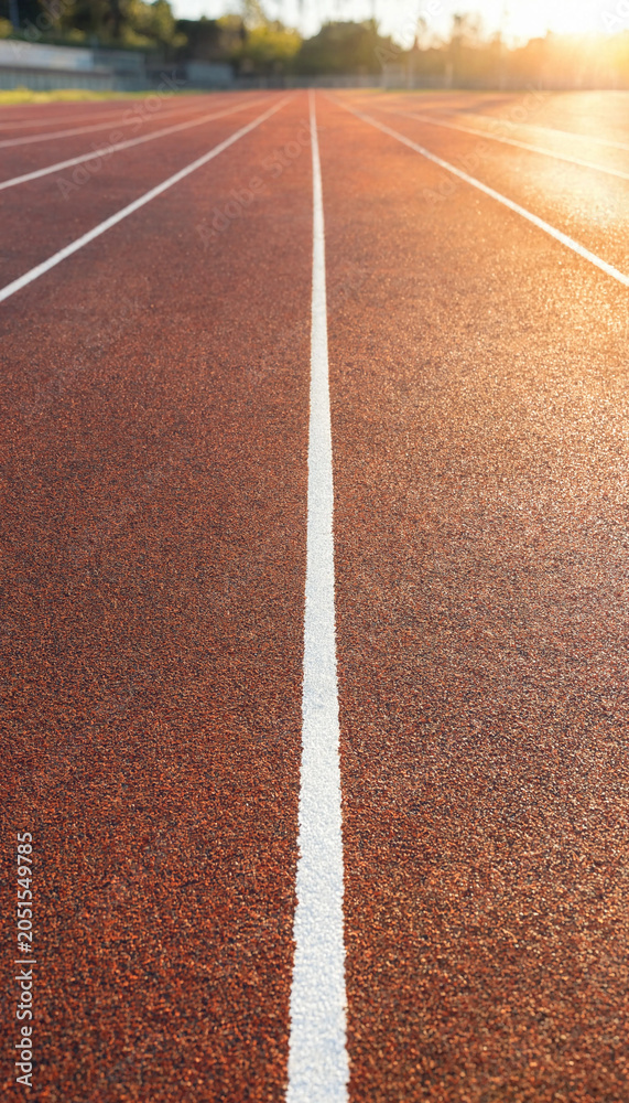 Fototapeta premium Running track lane surface with white markings lit by warm sunset light athletic exercise competition activity training sportswear marathon wellness challenge movement endurance