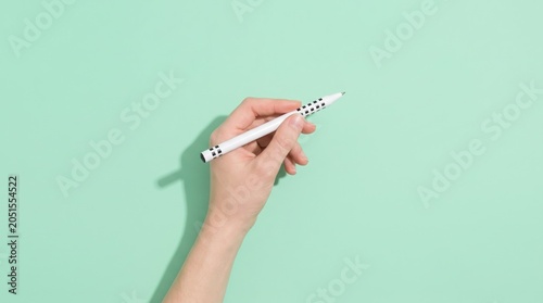 Hand holding a white pen with black checkered pattern against a pastel mint green background studio shot