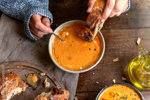 Bilde på lerret Person enjoying tomato soup with bread on a rustic wooden table.