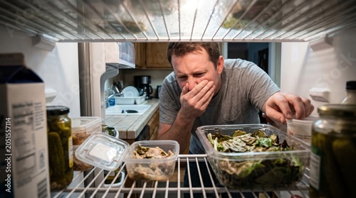 Man appears disgusted as he looks at spoiled food inside a refrigerator. Concept food waste, hygiene, home lifestyle, and freshness awareness. Perfect for illustrating food safety topics Generative AI