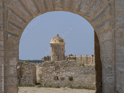Symmetrical framing of a medieval castle watchtower through an ancient stone arch in historic Siracusa, Italy. Beautiful architectural details of a Mediterranean coastal fortress.