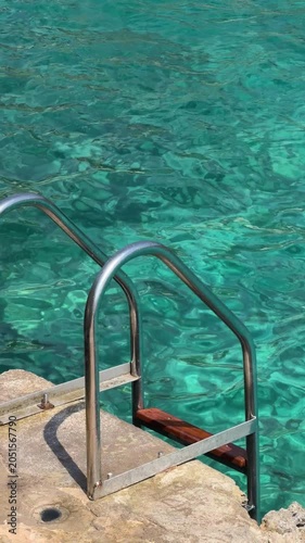 Metal ladder leading into crystal clear turquoise sea water, capturing a peaceful Mediterranean swimming spot on a sunny summer day in Mallorca.