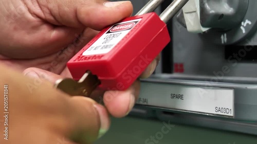 Industrial technician removing a Lockout Tagout padlock from an electrical isolation point after completing maintenance work, illustrating workplace safety procedures, energy control, and safe equipme
