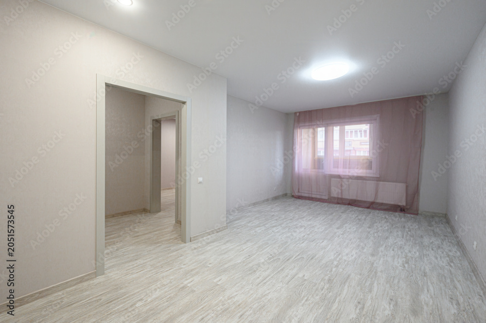 Fototapeta premium bright empty room with light beige walls, light wood laminate flooring, a window with sheer pink curtains, recessed ceiling lights, and an open doorway to another space