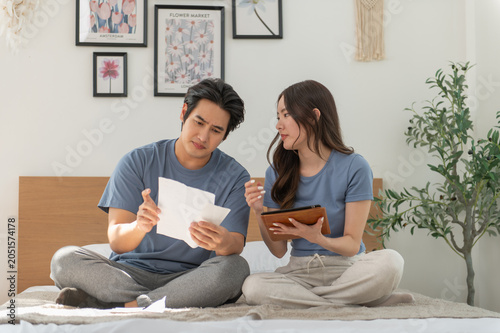Asian Couple reviewing bills feels stressed having financial problem, check finances, experiencing lack of money pay for loan, huge taxes, utility rates, get eviction notice.