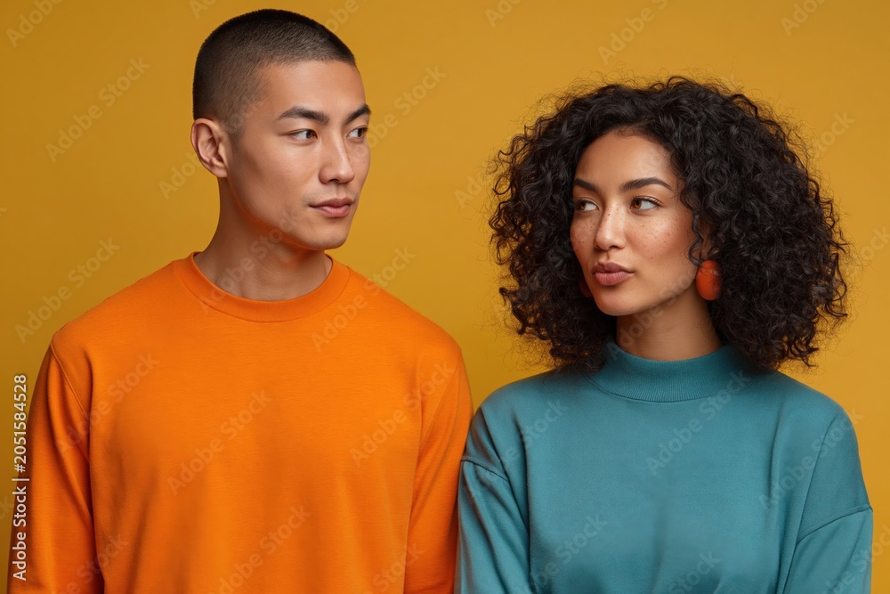 Fototapeta premium Young man and woman standing together in studio with colored backdrop