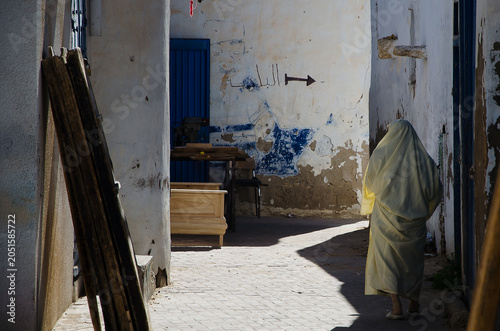 Fotografie Back view of a woman wearing traditional sefsari walking in a narrow alleyway in