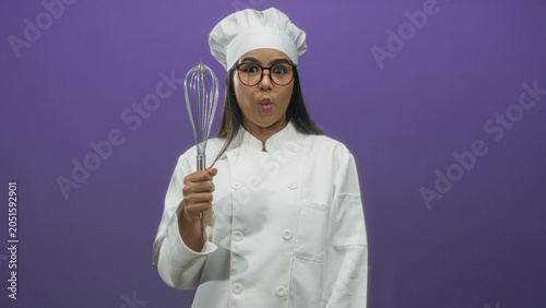 Bild auf Leinwand Young woman chef in white coat and hat holds whisk up and smiles toward camera in studio with purple backdrop, wearing glasses and showing varied playful expressions across frames; playful joy