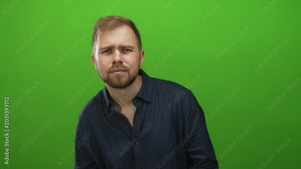 Naklejka premium Man tilts head, chest exposed and wearing dark blue shirt in studio with bright green backdrop; thoughtful introspection.
