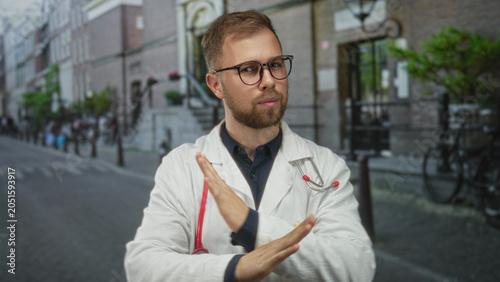 Canvas Print Man doctor with stethoscope crossing arms in x on street in city near bicycles and stone building facade; rejection professional caution
