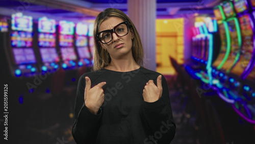Fotografie Woman with open palms raised by slot machines in casino building, wearing glasses and black top, looking upward; frustration