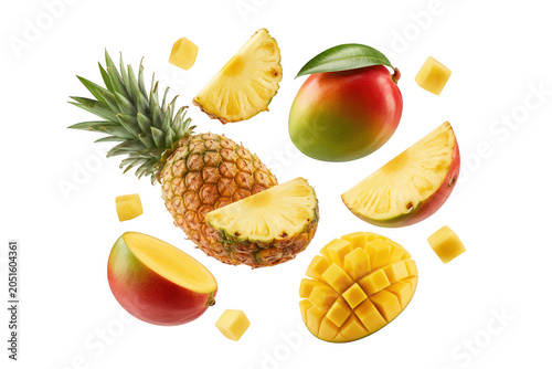 A fresh pineapple and juicy mango slices floating in the air with small fruit cubes scattered against a solid black background, for contrast