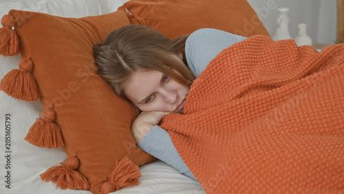 Bild auf Leinwand Woman lying on bed clutching orange blanket with hand to face, head on tassel pillow and subtle restless shifts in a domestic building bedroom set; quiet sadness