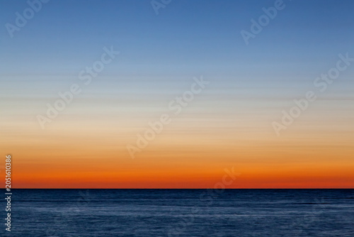 Clear and empty blue and orange gradient sky with copy space for background use, with horizon above a deep blue sea