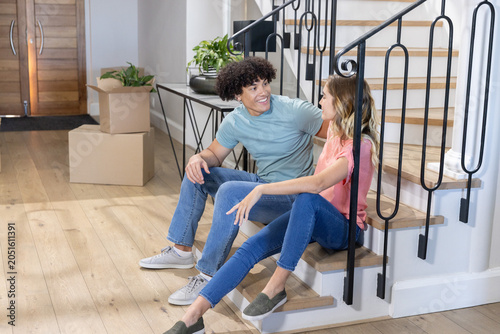Couple sitting on lower staircase steps talking near stacked moving boxes and potted plant