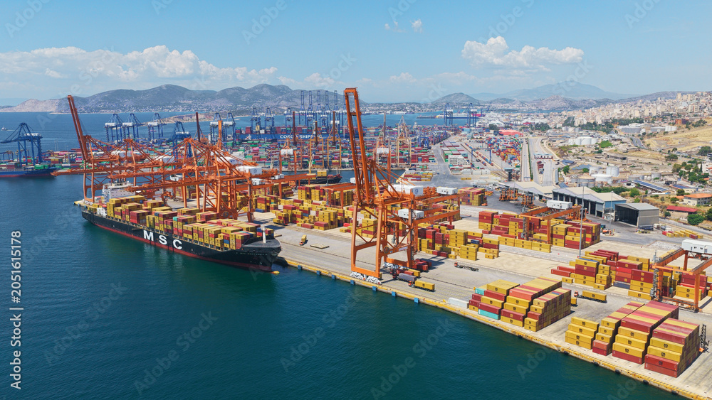 Obraz premium Large msc container ship docking at piraeus port amid stacked containers and gantry cranes, busy cargo terminal illustrating international shipping, logistics and trade operations