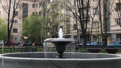 fountain stream gushes from a granite fountain bowl, cityscape