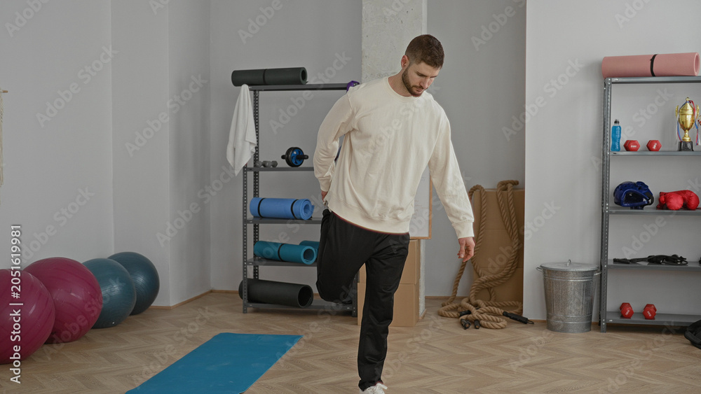 Fototapeta premium Man balancing on one leg on a yoga mat in a workout studio with exercise balls, ropes and dumbbells visible; focus balance calm.