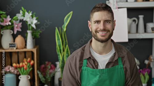 Tableau sur toile Young hispanic man florist wearing green apron smiling among flowers in a shop building; friendly service