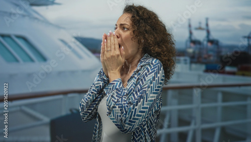 Foto Woman covering mouth with hands on cruise ship deck near railing and ship superstructure; alarm concern