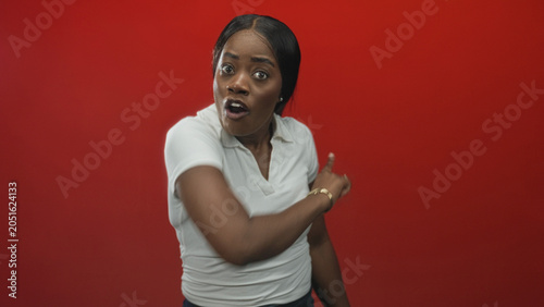 Foto Woman pointing arm forward in red studio with visible bare arm and urgent pointing gesture, mouth open in shock and motion blur; alarm accusation