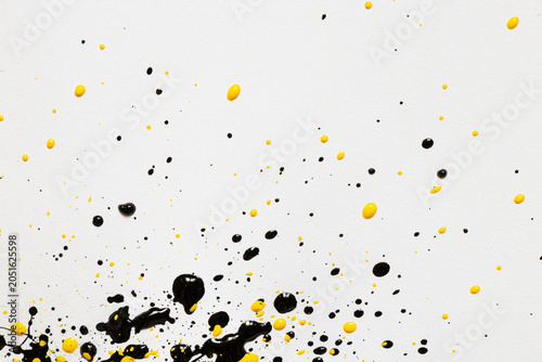 Yellow and black acrylic paint splashes on a white background with a contrasting texture and splatter effect