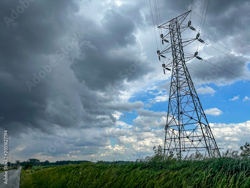Dark storm clouds over a rural field and road by a high voltage electricity transmission tower in the American midwest