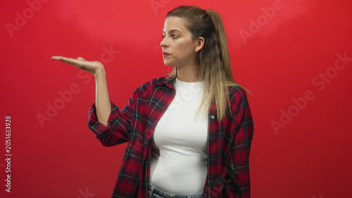 Foto Woman hands raised, shoulder shrug gesture wearing red plaid shirt and white tee in studio against red backdrop; casual uncertainty