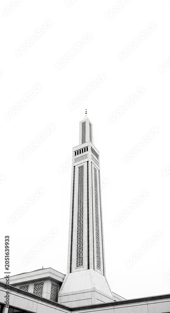 Obraz premium A tall, slender minaret of a mosque rendered in stark black and white, featuring a square base, multiple levels with decorative geometric latticework, and a pointed spire, set against a