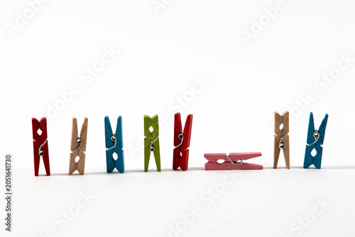 A row of colorful small wooden clothespins standing vertically with one pink peg lying horizontally on a textured white background