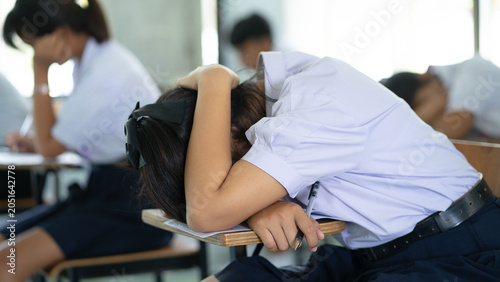 Exhausted Female Student Sleeping on Desk During Final Exam in Classroom