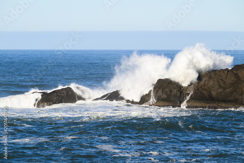 White ocean waves break over coastal rocks with calm sea and horizon