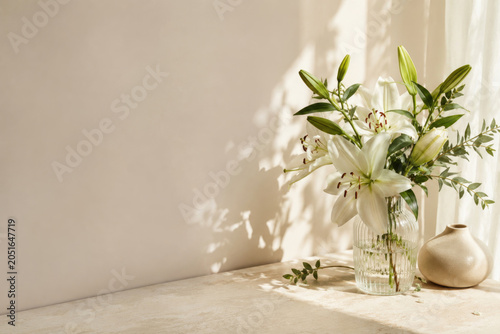 White lilies in glass vase beside ceramic vessel. Space for text.