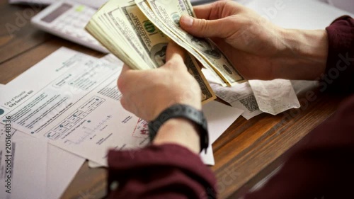 At his desk, an aspiring entrepreneur tallies cash beside unpaid bills, using a calculator to gauge start-up capital. This moment captures early financial planning for launching a new business