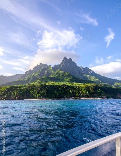 A serene tropical landscape with a mountainous island in the background, lush greenery, and deep blue waters