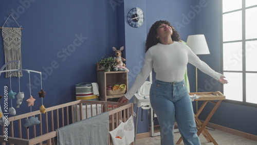 Foto Woman leans over wooden crib touching hanging mobile and adjusting blanket with hand in baby room studio; tenderness