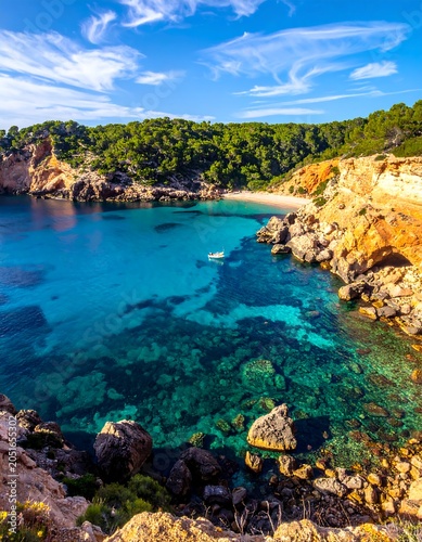 A serene turquoise cove nestled among rugged cliffs and lush greenery under a vibrant blue sky