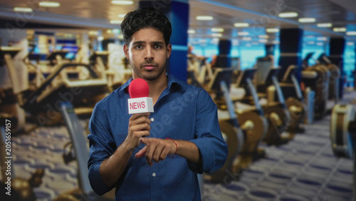 Foto Man holding red microphone labeled news and pointing finger in gym building while wearing blue shirt; press urgency
