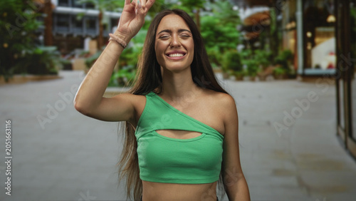 Φωτογραφία Woman making rock horns gesture on a city street showing exposed midriff and smiling expression; joy fun energy youthful