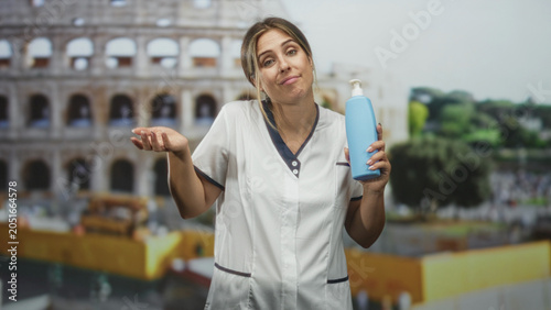 Foto Woman nurse in white coat holds blue pump bottle and shrugs shoulders in front of colosseum backdrop in a studio; bemusement uncertainty resignation doubt