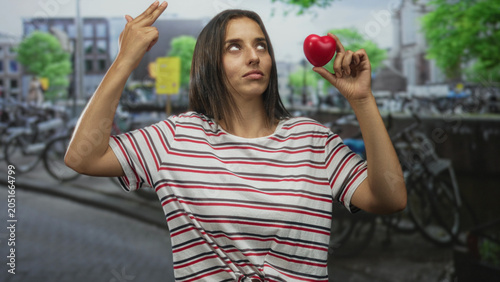 Photos Woman holding red heart and pointing two fingers upward on a street in amsterdam; love irony sarcasm
