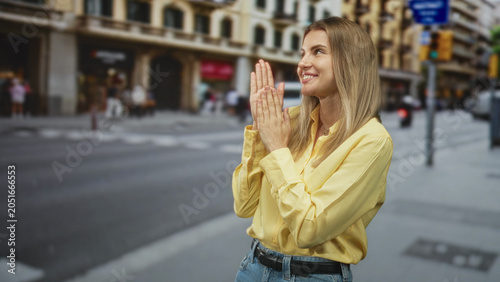 Foto Blonde woman pressing hands together in a pleading prayer pose on a busy street crosswalk by shops and a white van; hopeful