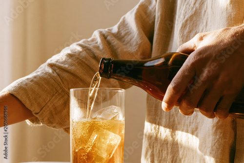 Pouring glass ice close up shot arm linen shirt hand bottle liquid into glass with ice warm light and mist
